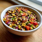 Close-up of a vibrant cowboy caviar recipe featuring black-eyed peas, corn, tomatoes, and red onion in a white bowl.