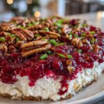 Close-up of a layered cranberry cream cheese dip topped with whole pecans and chopped green onions.