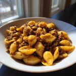 A white bowl filled with creamy beef pasta featuring shell-shaped noodles coated in a rich, savory sauce.