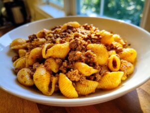 Close-up of a white bowl filled with creamy beef pasta featuring shell-shaped noodles and seasoned ground beef.