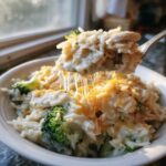 A spoonful of creamy crockpot chicken and rice with melted cheese stretching between the spoon and the bowl.