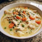 Close-up of creamy pot pie soup filled with shredded chicken, carrots, peas, and fresh thyme.