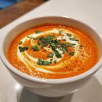 Close-up of creamy tomato basil soup topped with a swirl of cream and fresh chopped basil.