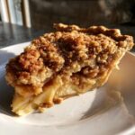 Close-up of a slice of dutch apple pie recipe showing thick apple filling and a crunchy cinnamon streusel topping.