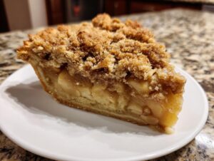 A close-up of a slice of dutch apple pie recipe featuring thick apple filling and a crunchy brown sugar crumb topping.