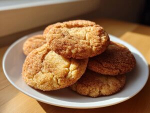 A stack of freshly baked churro cookies coated in cinnamon sugar resting on a white plate.