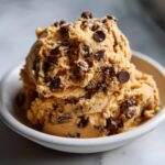 Two scoops of rich, edible chocolate chip cookie dough recipe served in a small white bowl.