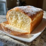 A loaf of fluffy, golden condensed milk bread with a slice cut, dusted with powdered sugar.