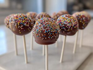 A close-up of several chocolate-dipped cake pops topped with colorful sprinkles, ready to serve.