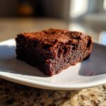A close-up of a fudgy, rich slice of date brownies resting on a white plate.