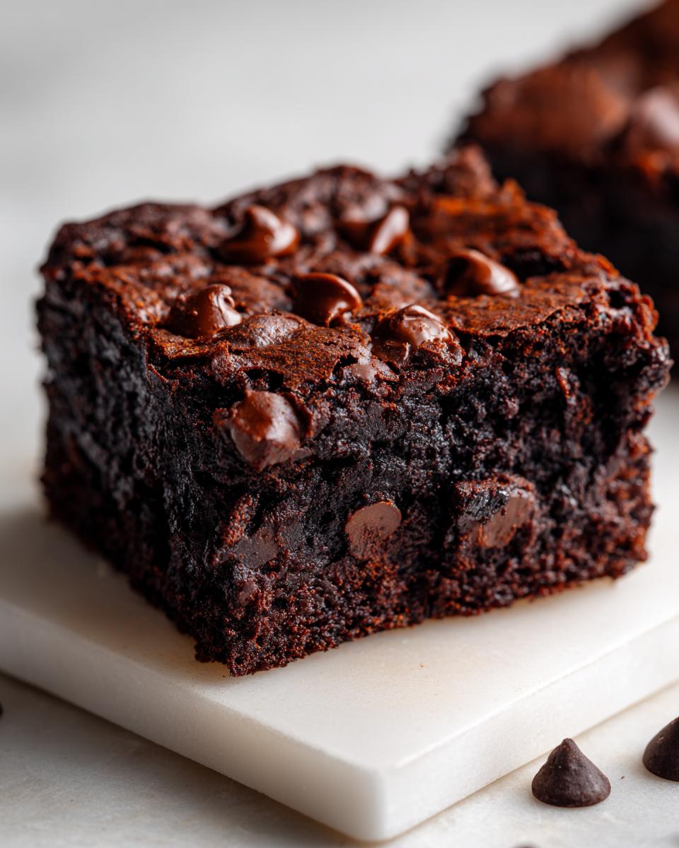 Close-up of a fudgy square of zucchini brownies topped with melted chocolate chips.