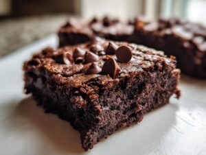 Close-up of a fudgy zucchini brownies square topped with melted chocolate chips on a white plate.