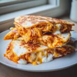 Stack of gooey, cheesy buffalo chicken quesadilla wedges overflowing with filling and sauce.