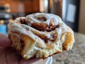 A close-up of a gooey cinnamon roll being held, showing the soft interior and thick white icing.