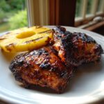 Two pieces of juicy hawaiian huli huli chicken with a dark, sticky glaze served next to a slice of grilled pineapple.