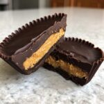 Close-up of homemade peanut butter cups cut in half, showing thick chocolate shell and creamy peanut butter filling.