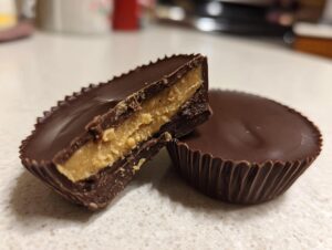 Close-up of homemade peanut butter cups, one cut in half showing the thick peanut butter filling inside the chocolate shell.