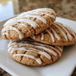 Three soft maple brown sugar cookies stacked on a white plate, drizzled with white icing.