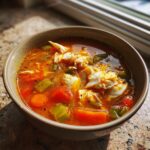 A close-up of a bowl of rich, red maryland crab soup filled with large chunks of white crab meat, carrots, and celery.