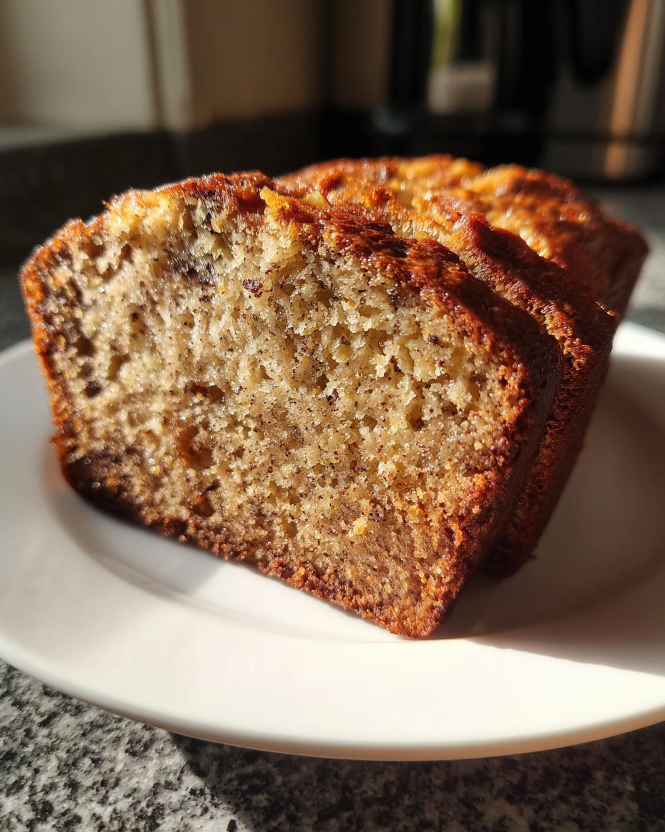 Close-up of two thick slices of moist banana bread recipe on a white plate, showing the speckled crumb texture.