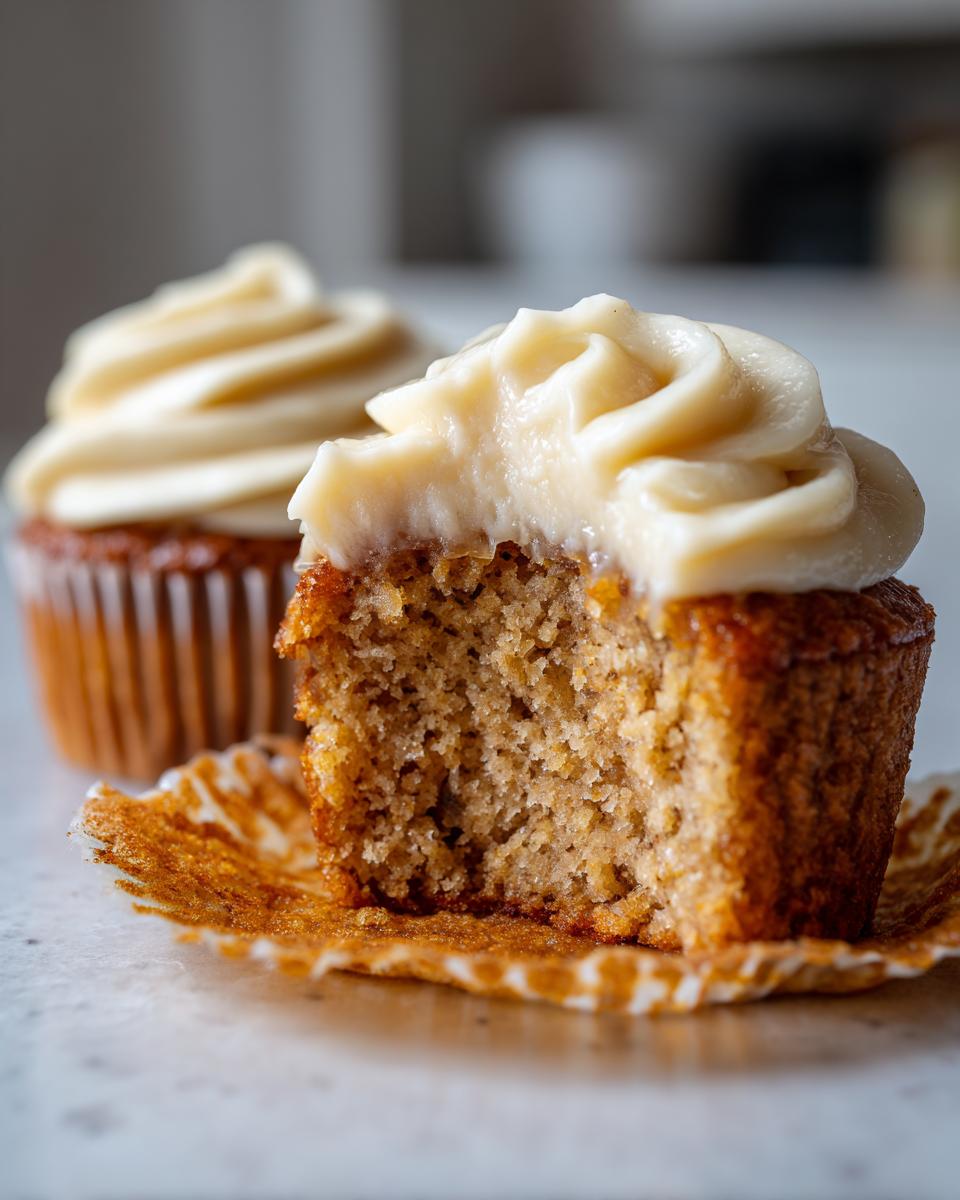 Close-up of a banana cupcakes cut in half showing the moist crumb and thick cream cheese frosting.