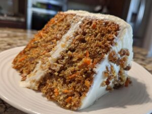Close-up of a thick slice of moist carrot cake layered with rich cream cheese frosting.