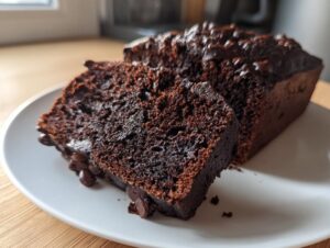 Close-up of a moist slice of dark chocolate zucchini bread with visible chocolate chips on a white plate.