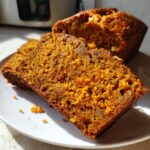 Close-up of two moist, orange-hued slices of persimmon bread on a white plate.