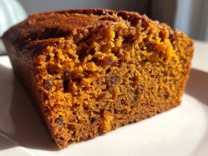 Close-up view showing the moist, orange-hued crumb texture of the baked persimmon bread with visible dark fruit pieces.