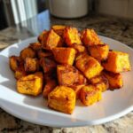 A pile of perfectly caramelized, cubed roasted sweet potatoes served on a white plate.