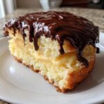 A close-up slice of moist Boston cream pie featuring vanilla cake, pastry cream filling, and dripping chocolate ganache.