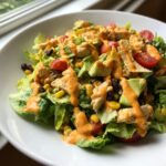 Close-up of a vibrant southwest salad featuring chicken, avocado, corn, black beans, and a creamy orange dressing.