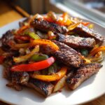 Close-up of perfectly grilled, sliced steak fajita mixed with colorful sautéed bell peppers and onions on a white plate.