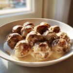 Close-up of delicious Swedish meatballs generously covered in rich, creamy brown gravy in a white bowl.