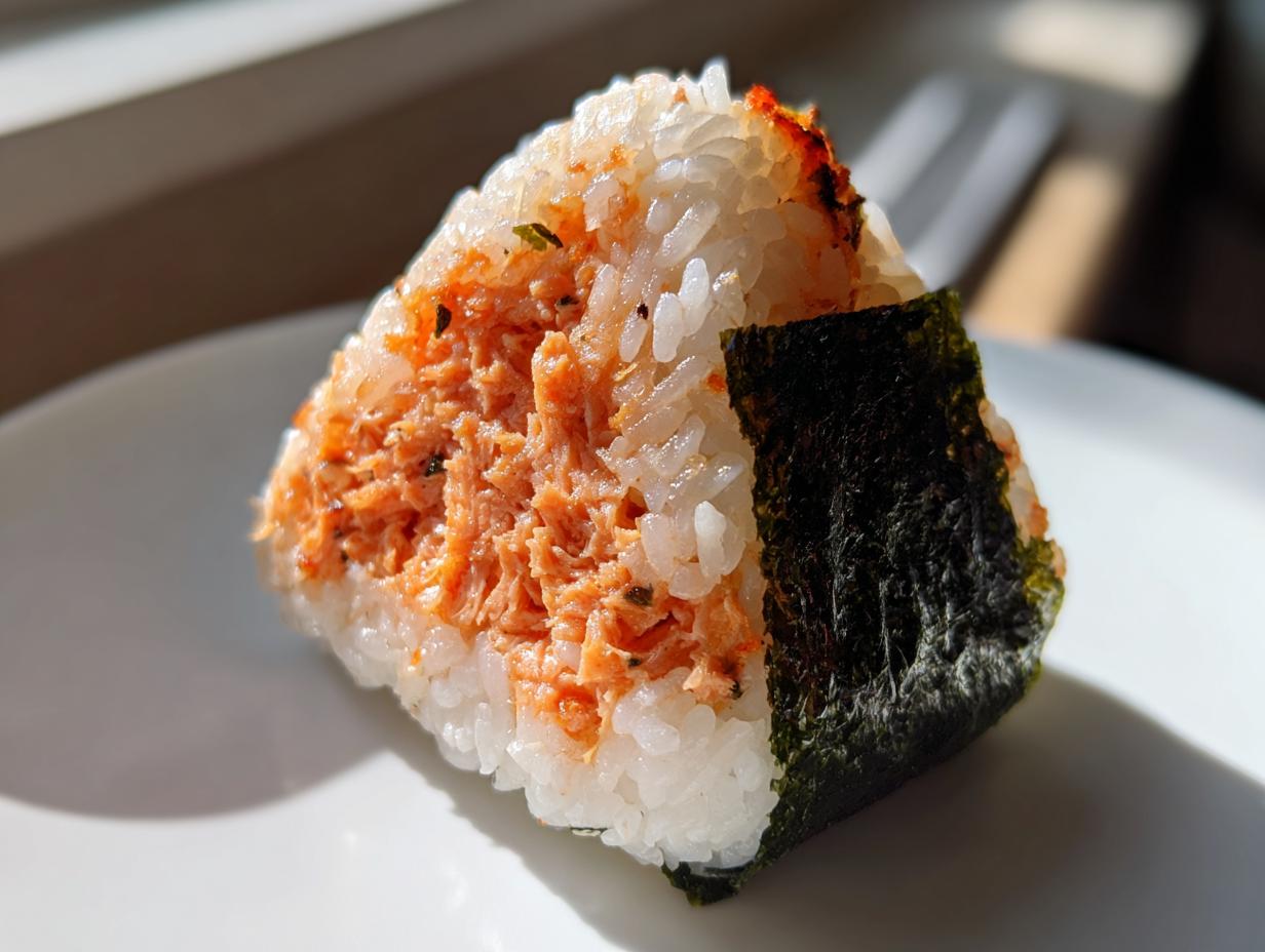 Close-up of a triangular tuna onigiri rice ball showing the orange tuna filling and a piece of dark nori seaweed.