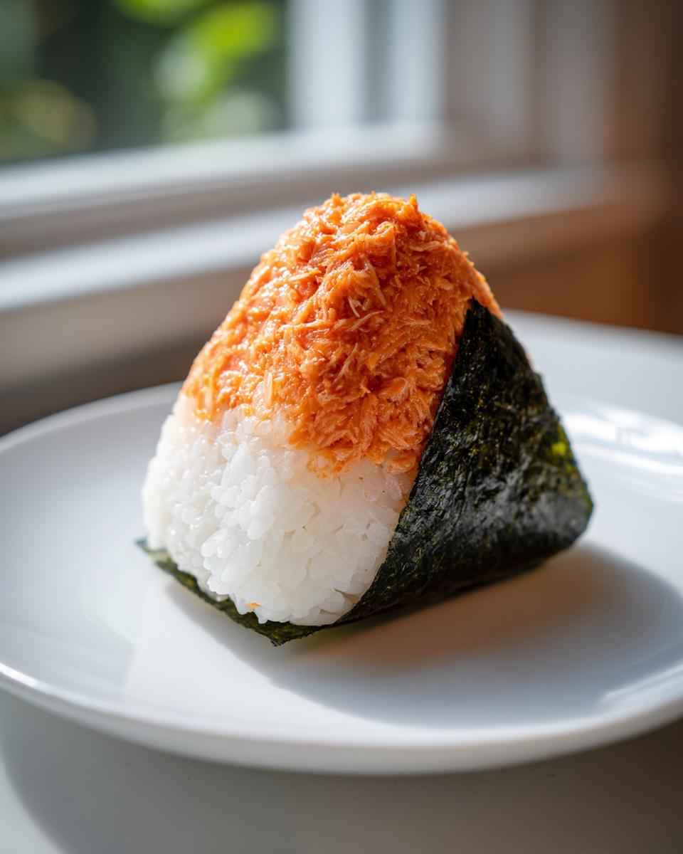 A single, triangular tuna onigiri featuring white rice topped with seasoned tuna filling and wrapped with a strip of nori seaweed.