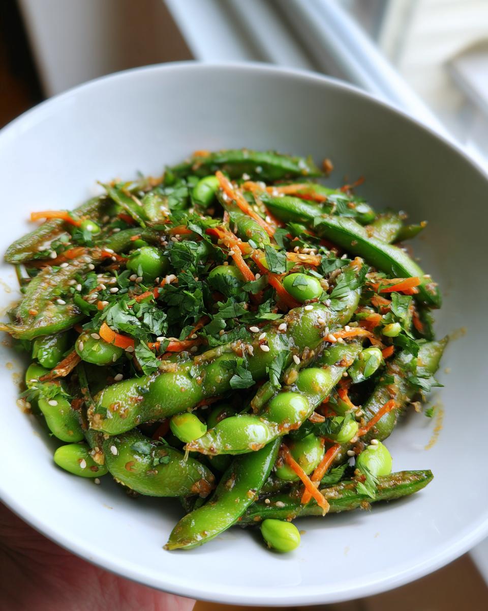 Close-up of a vibrant edamame salad featuring pods, shelled beans, shredded carrots, and sesame seeds.