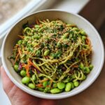 A close-up of a vibrant edamame salad featuring spiralized vegetables, shelled edamame, and sesame seeds.