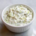 Close-up of creamy, chunky homemade tartar sauce recipe in a small white fluted bowl.