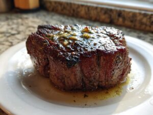 Close-up of a thick, juicy air fryer steak resting on a white plate, glistening with melted garlic herb butter.