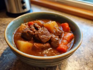 Close-up of a bowl filled with rich, dark brown beef stew featuring tender chunks of beef, potatoes, and bright orange carrots.