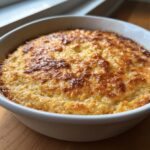 Close-up of a freshly baked, creamy corn dip in a white round baking dish, featuring a beautifully browned, cheesy top.