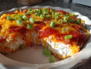 A portion removed from a baked cream cheese dip topped with melted cheddar, sauce, and green onions.