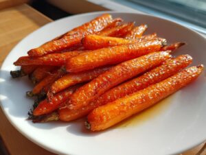 A pile of perfectly glazed and caramelized roasted carrots served on a white plate, highlighted by sunlight.
