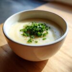 A close-up of creamy roasted cauliflower soup topped with fresh green parsley and pepper.