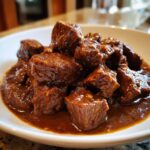 Close-up of tender crockpot beef tips smothered in a thick, dark brown savory sauce served in a white bowl.