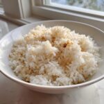 A close-up of fluffy white butter rice topped with browned garlic or seasonings in a white bowl.