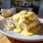 Close-up of sliced meat topped with poached eggs and a generous pour of bright yellow hollandaise sauce, sprinkled with paprika.