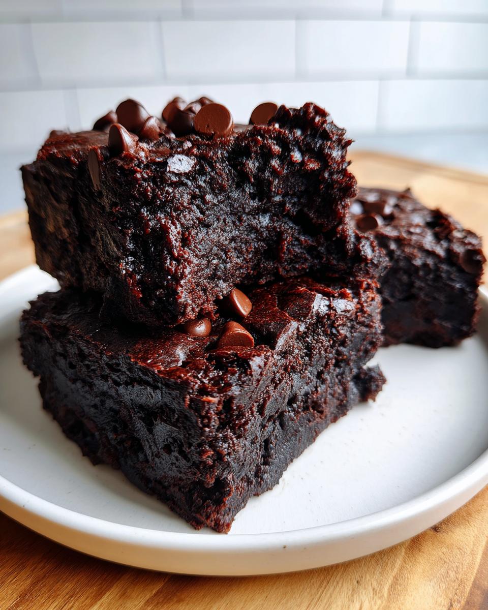 Close-up of stacked, fudgy black bean brownies topped with chocolate chips on a white plate.
