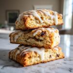 Three square chocolate chip scones stacked vertically, drizzled with white vanilla glaze.